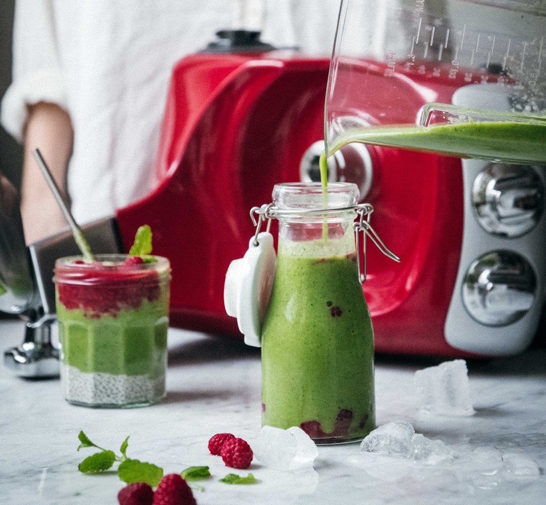 En kvinna häller en grön smoothie i en glasburk.