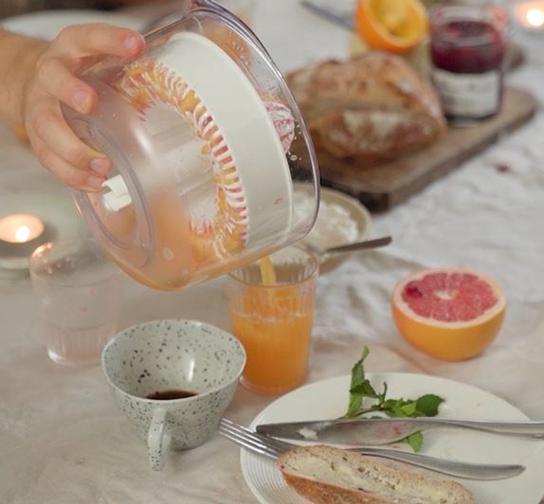 En person häller juice i ett glas på ett bord med frukost.