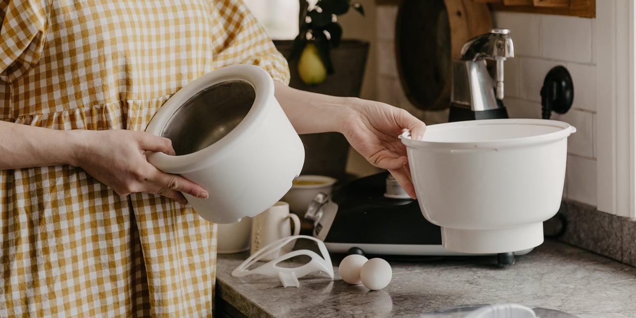 A woman holding a ice cream mixer bowl in the kitchen.