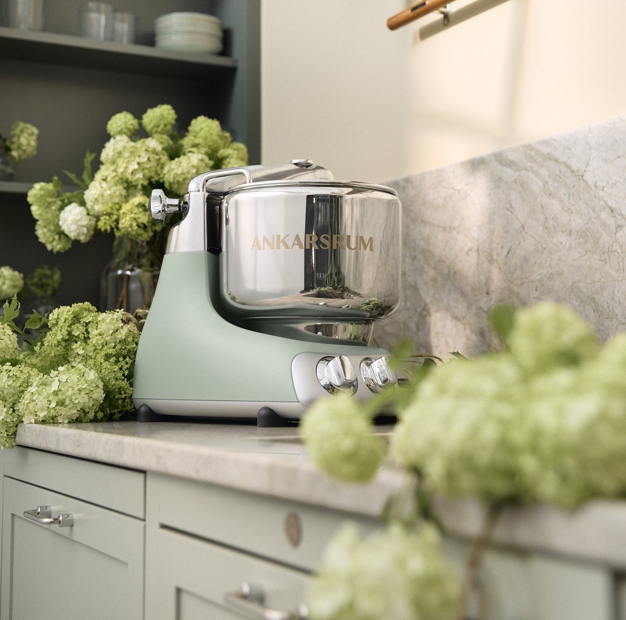 A green mixer sitting on top of a kitchen counter. With flowers on the side