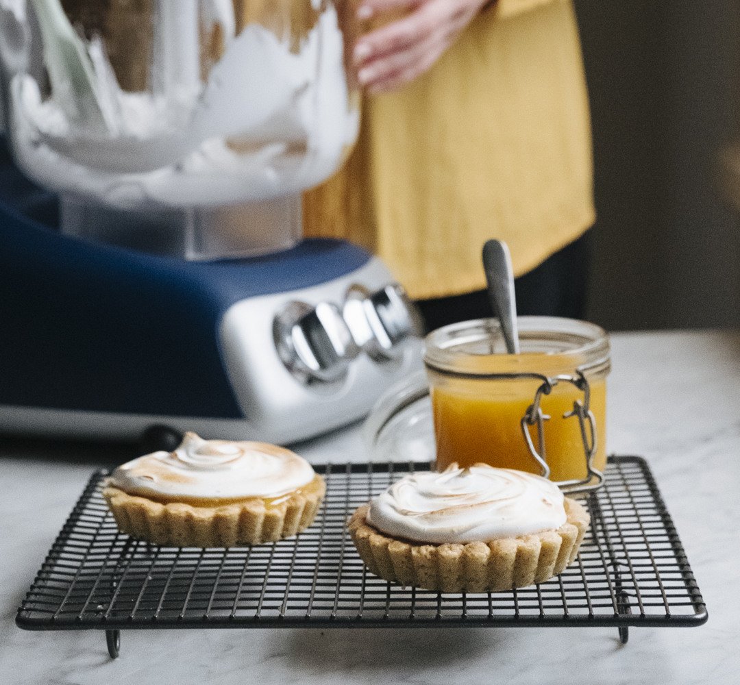 Ett par cupcakes som står på ett avsvalningsgaller. Ankarsrum assistent och en person i bakgrunden.