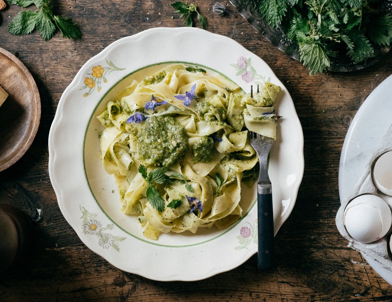 A plate of nettle pesto pasta on a wooden table, with a fork twirling some of the pasta.