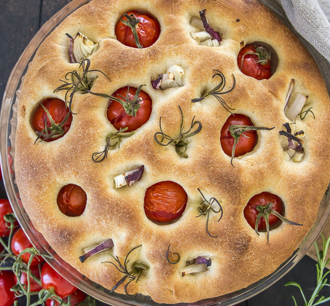 Gyllene-brun focaccia med tomater och röd lök på ett bord.