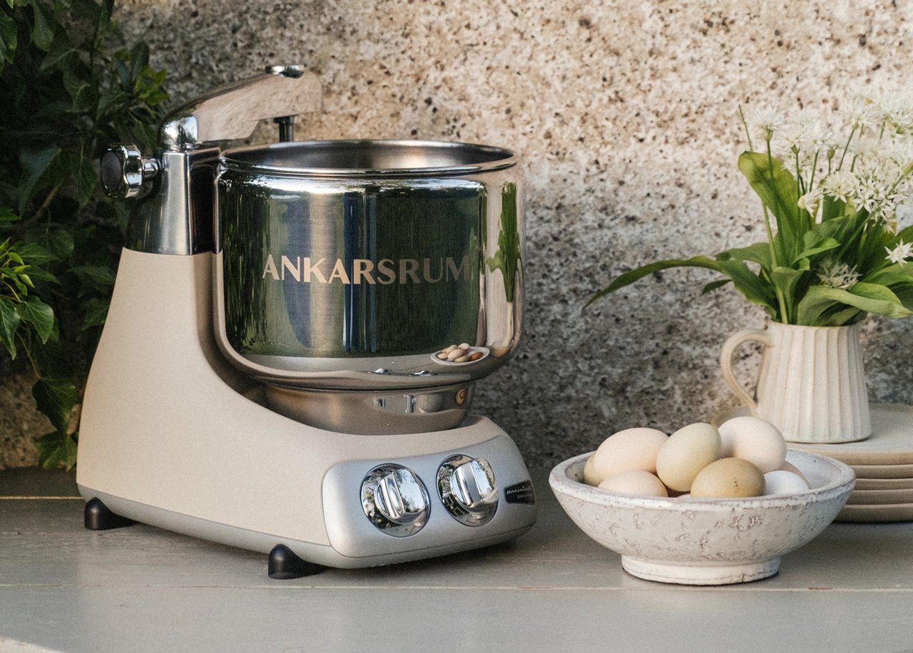 A table with a bowl of eggs and a ankarsrum assistent on it. Plants in the background.