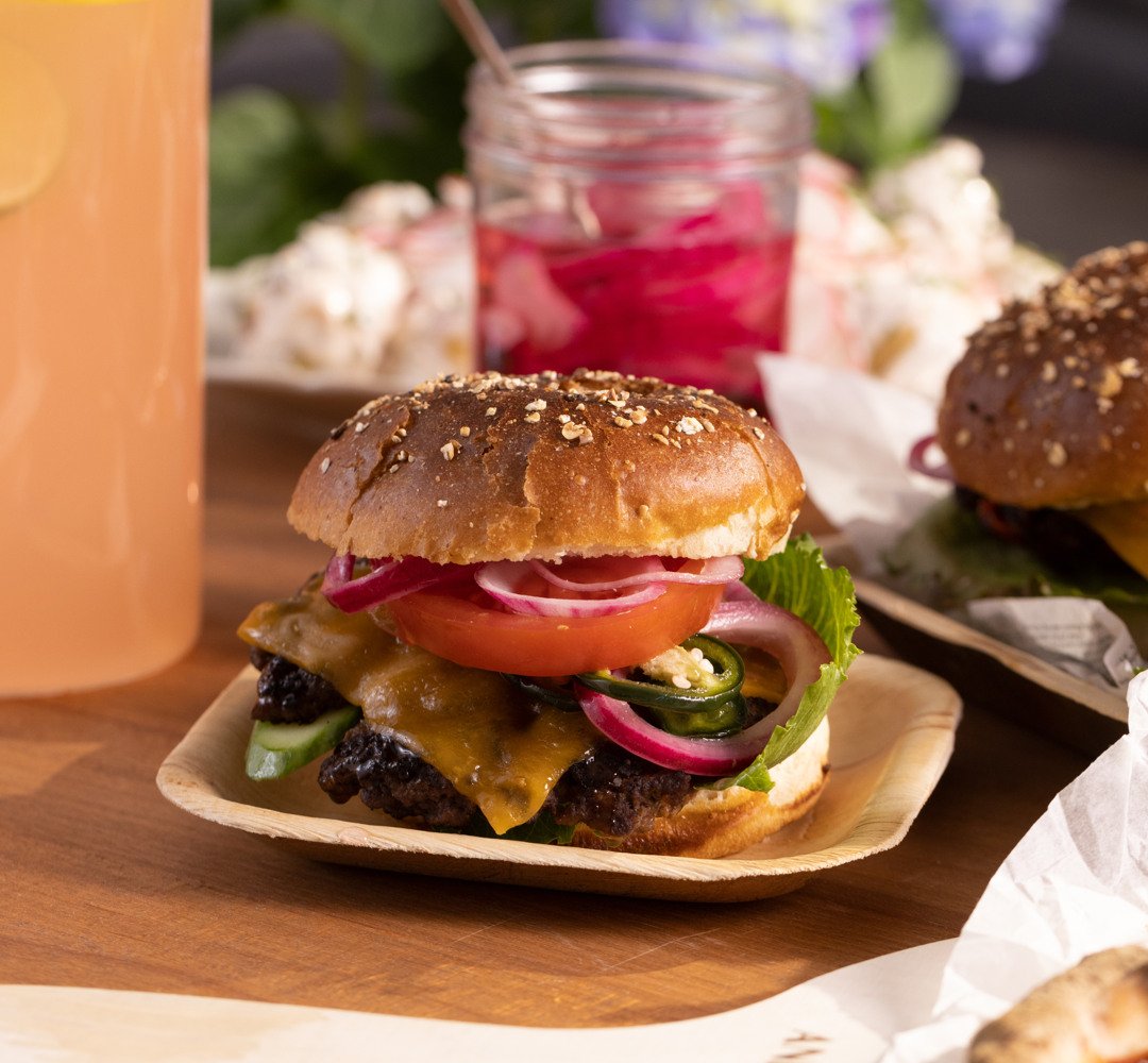 Smashed burger hampurilaissämpylässä, jossa on salaattia, tomaattia ja punasipulia. Pöydällä.