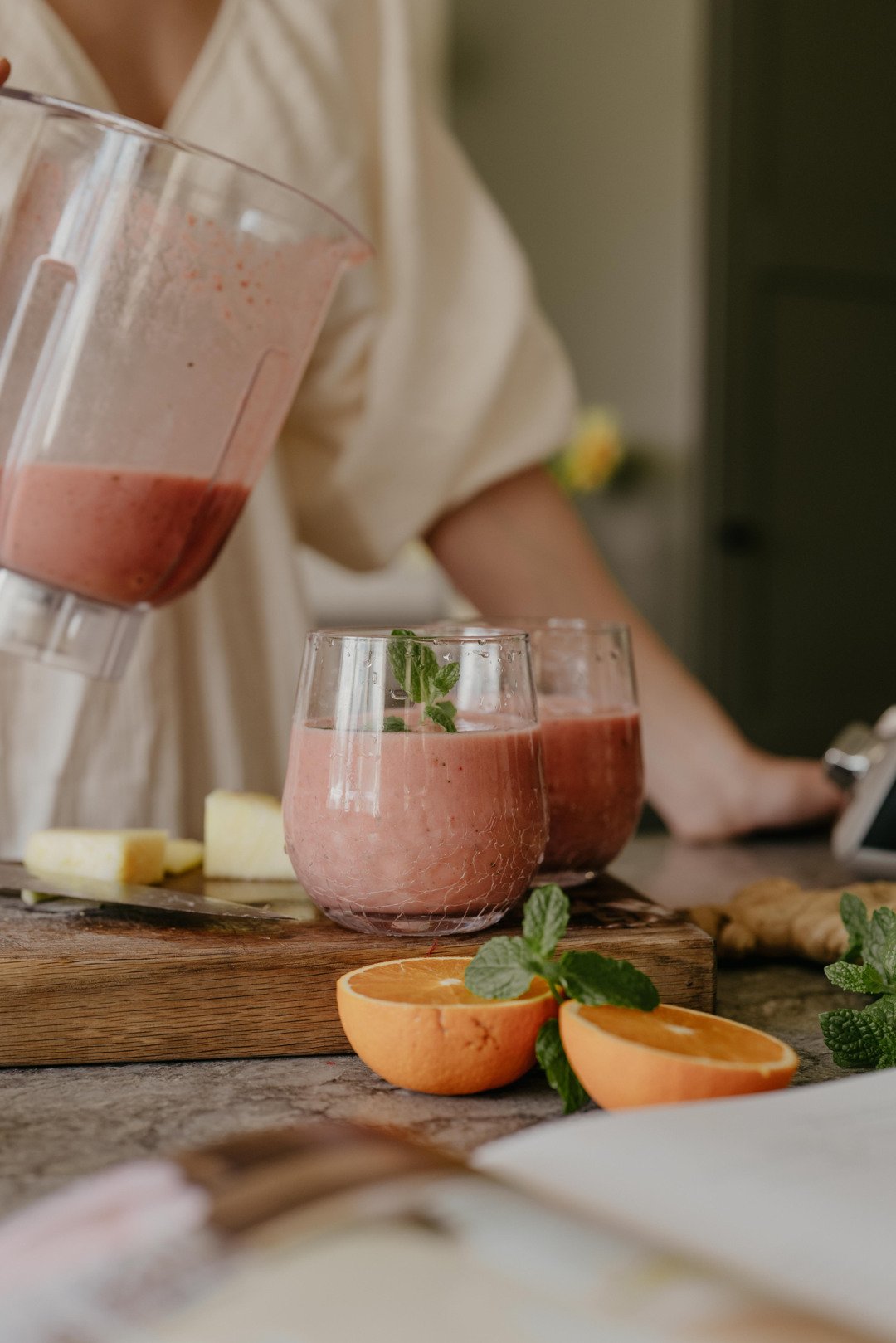 Häller en nyblandad bärsmoothie i glas med hjälp av Ankarsrum-blendertillbehöret, omgiven av färsk frukt och örter.