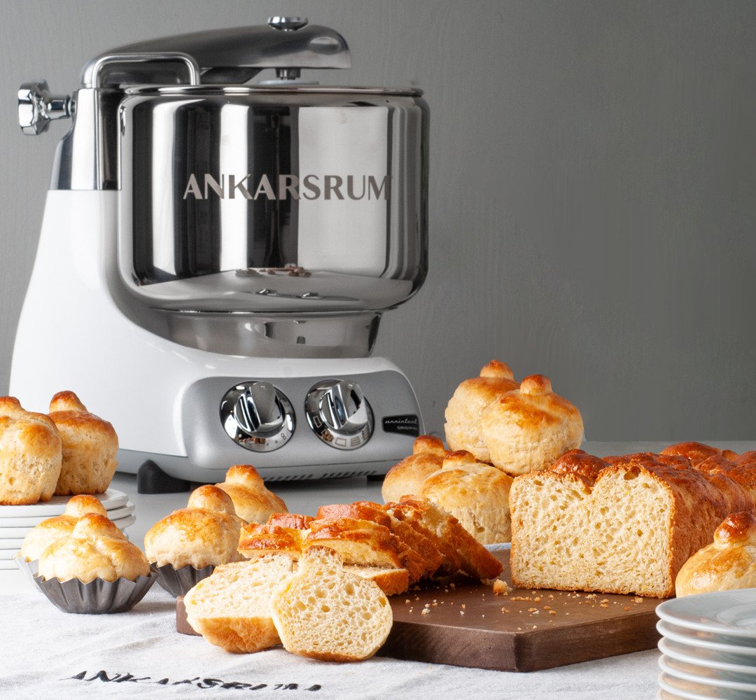 A bunch of bread that is on a table. ankarsrum assistent in the background