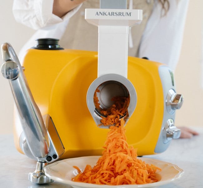 A woman is cutting carrots in ankarsrums vegetable cutter