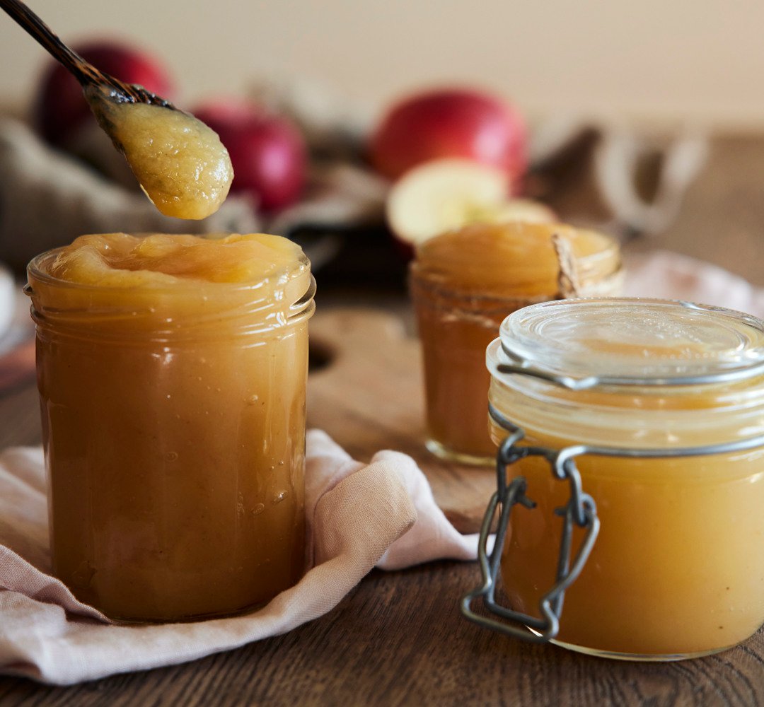 Applesauce in glass jars, with red apples placed behind the jars.