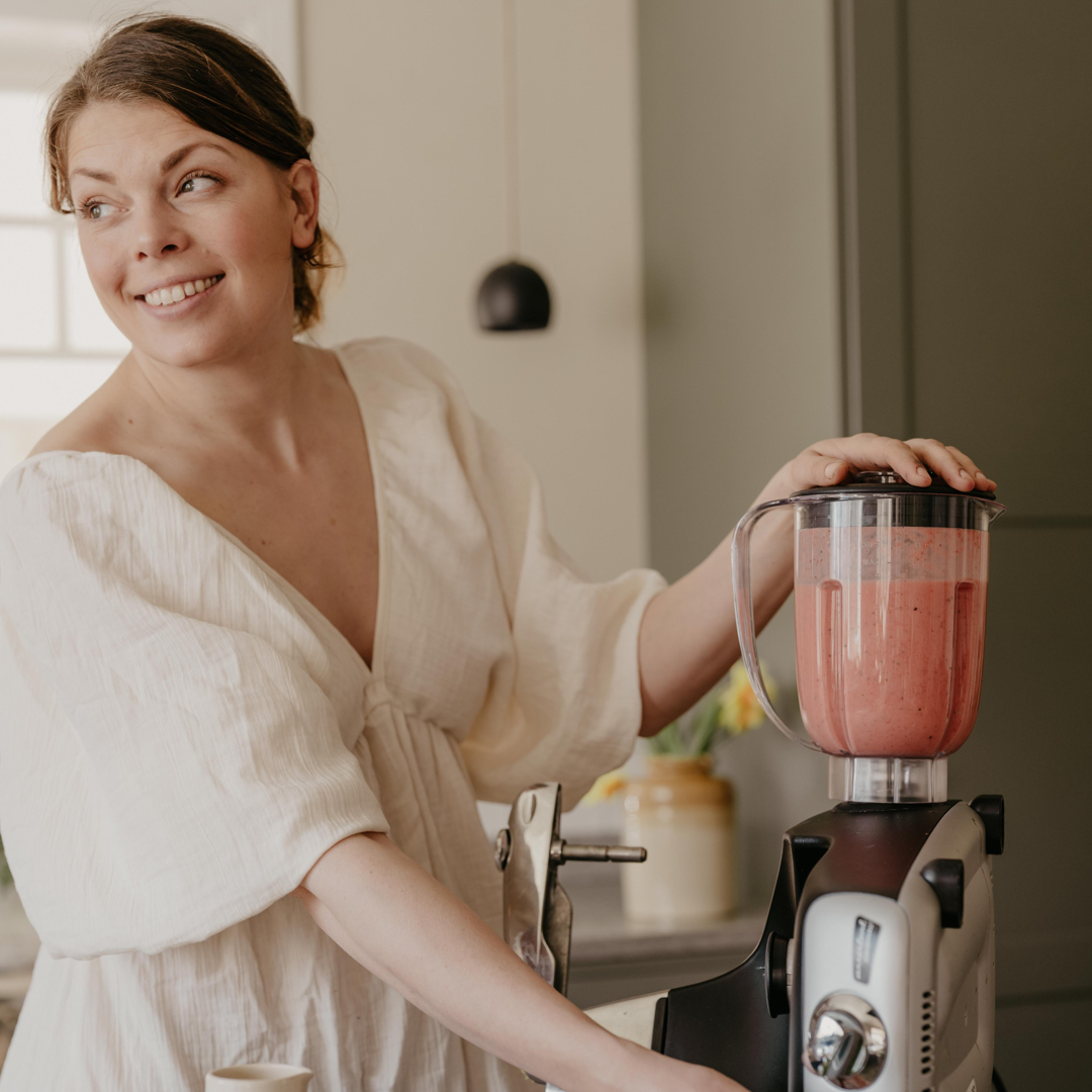 Kvinna som gör en bärsmoothie med en Ankarsrum Assistent Original utrustad med en mixer i ett ljust, modernt kök.
