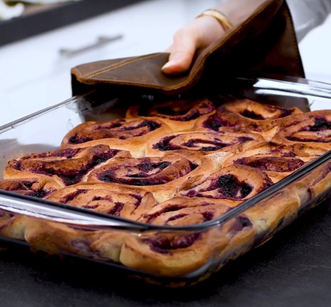 A person placing blueberry buns in a glass dish.