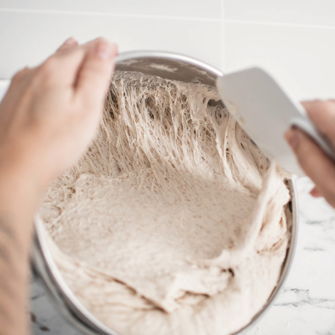 A person mixing a bowl of dough with a spatula.