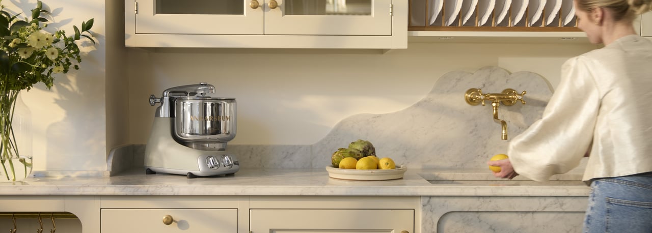 An Ankarsrum Assistent Original in Harmony Beige on a marble kitchen worktop in a bright kitchen.