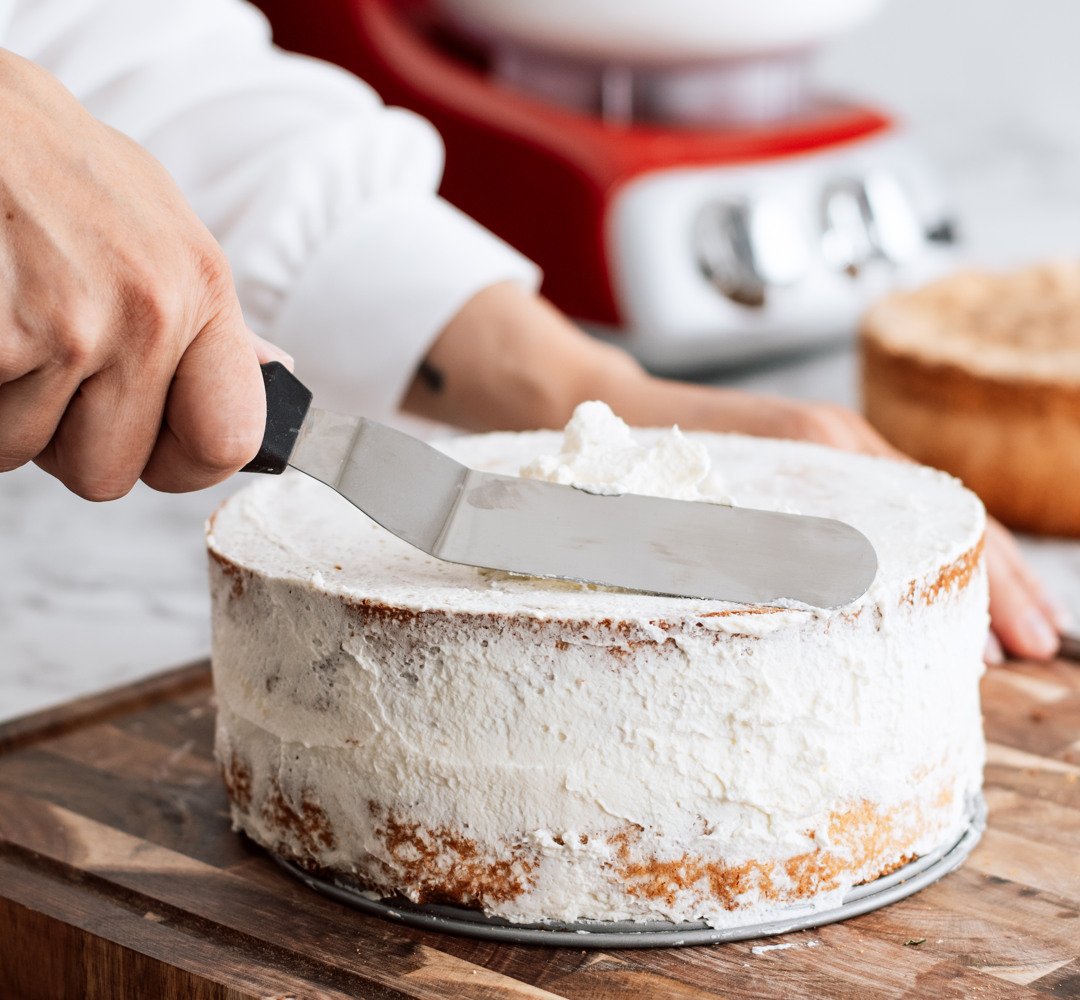A person spreading whipped cream on a cake.