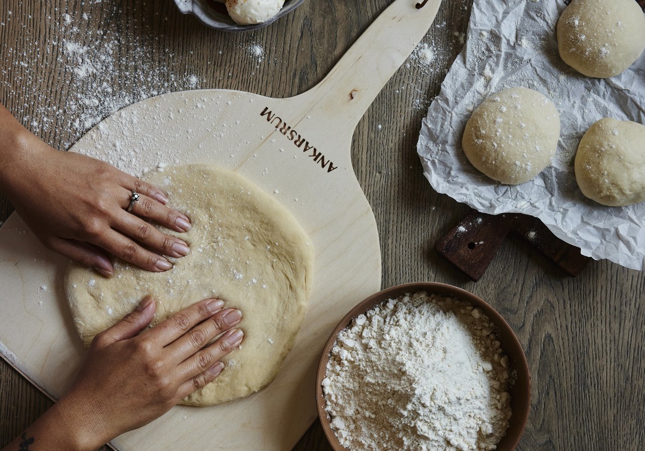 A person kneading dough on top of a wooden table.