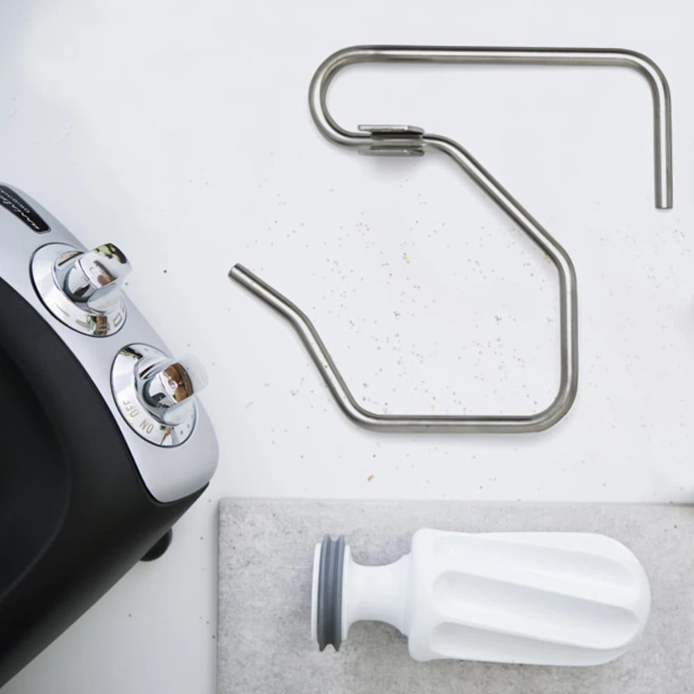 Dough roller and dough hook lying on a light-coloured table, with a black Ankarsrum Assistent visible beside them.