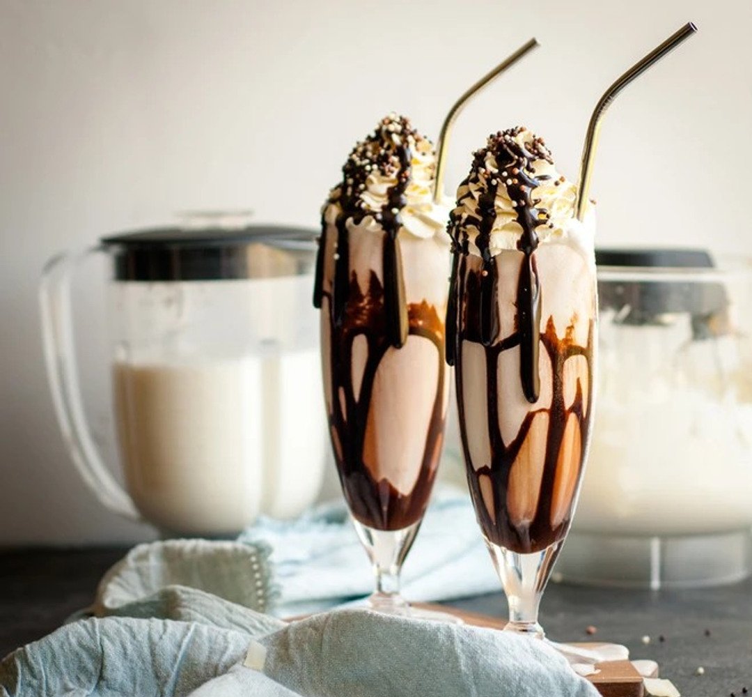 Två glas fyllda med milkshake toppat med grädde och chokladsås
