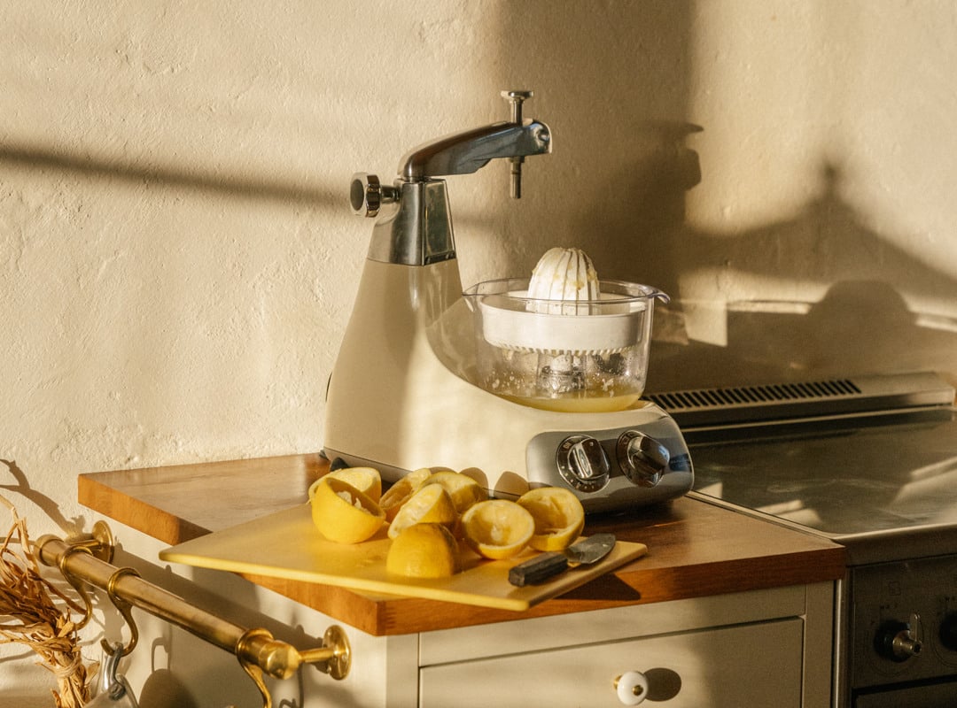 En köksbänk med citroner och en ljus cremefärgad stående mixer med en citruspress-tillbehör.