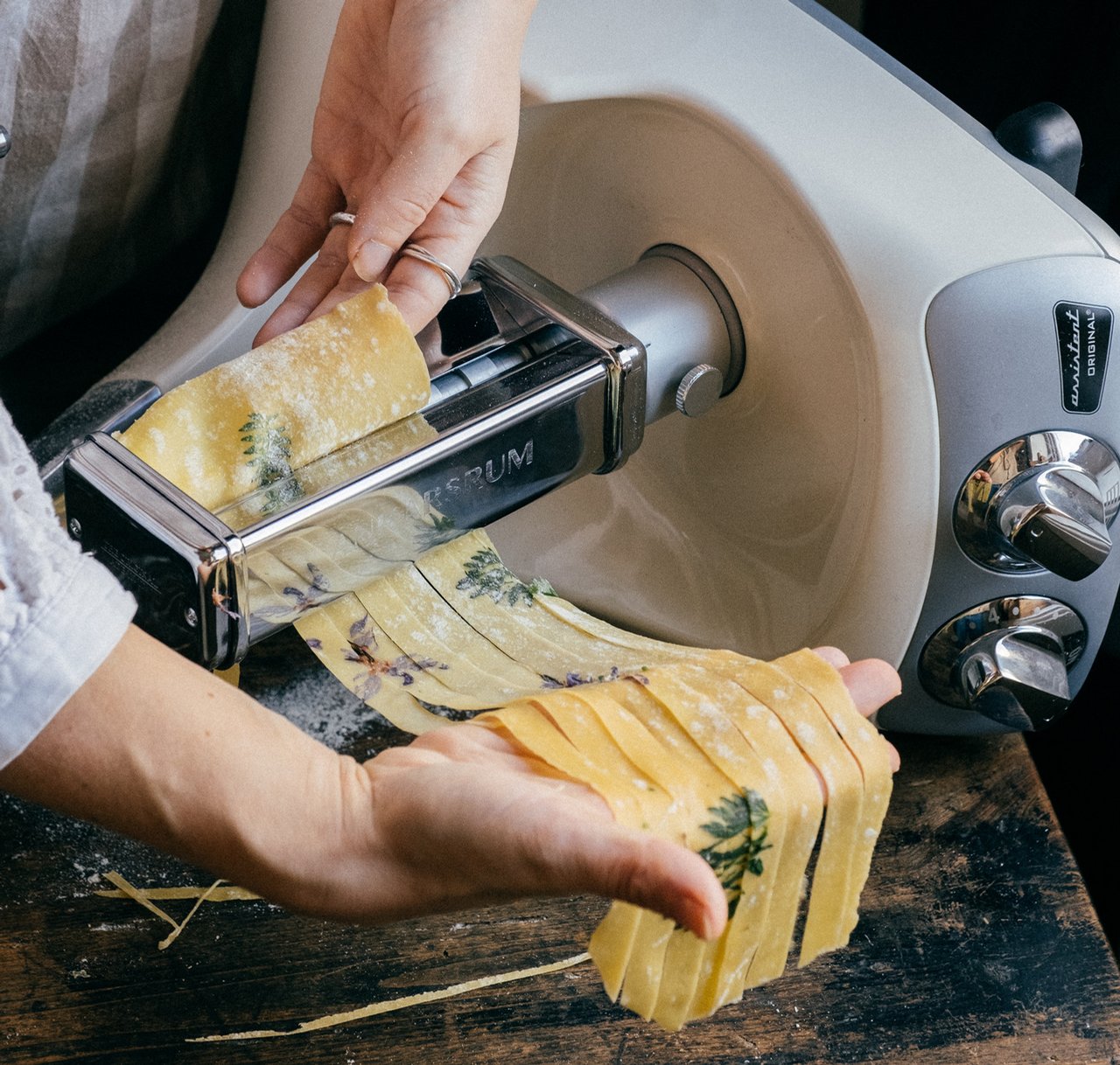 A person is making fettuccine pasta using the pasta attachment on an Ankarsrum Assistent.