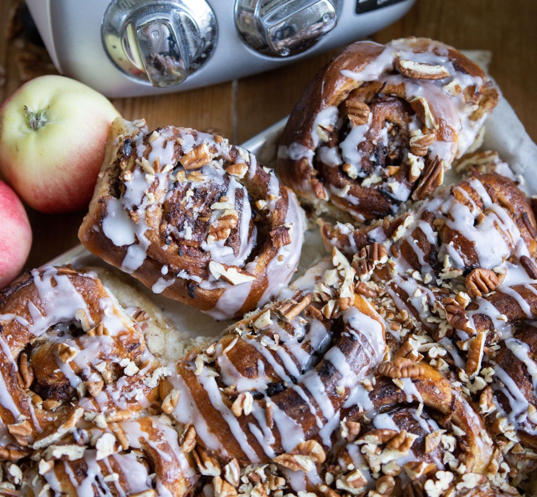 A plate of buns that is on a table. With apples on the side