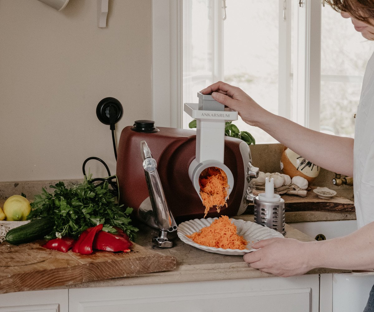 A woman standing in a kitchen cutting greens in the vegetable cutter