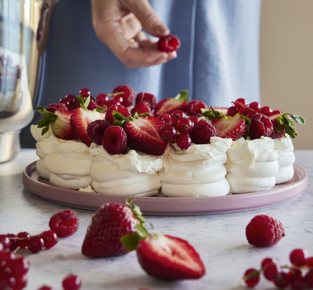 Pavlova på ett bord med en person som lägger till hallon.