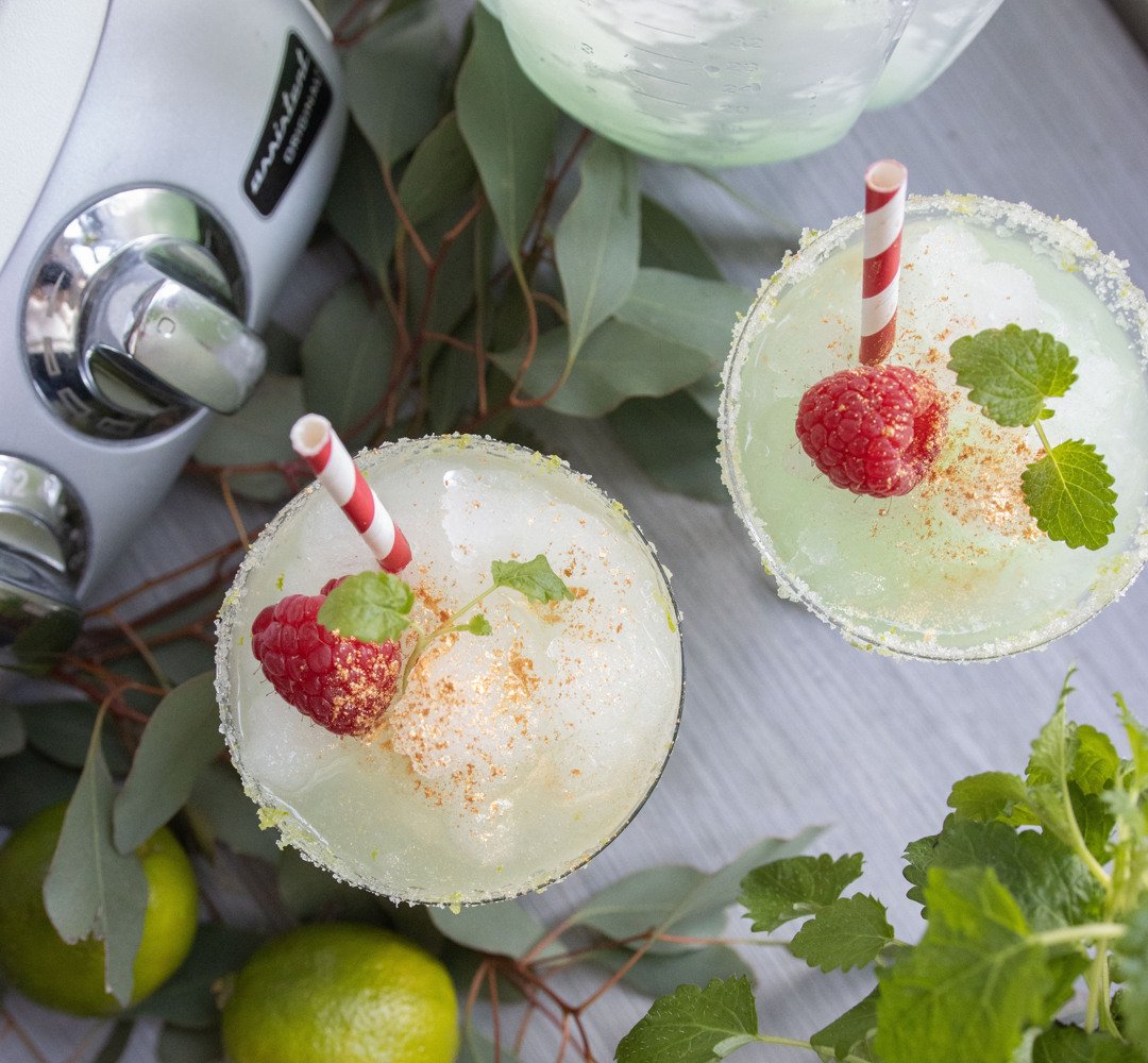 Två margaritas med jordgubbar och garnering på ett bord.