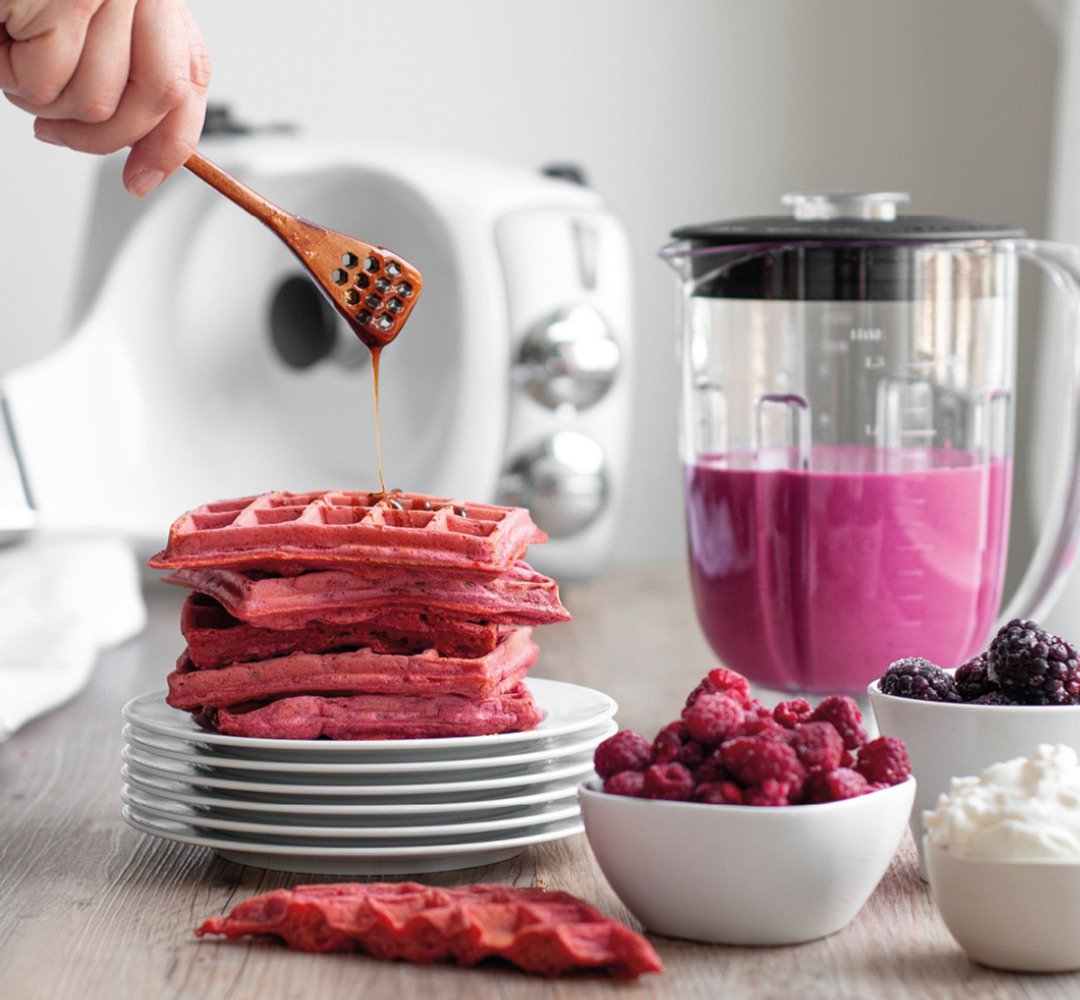 A person drizzling something into a plate of pink waffles