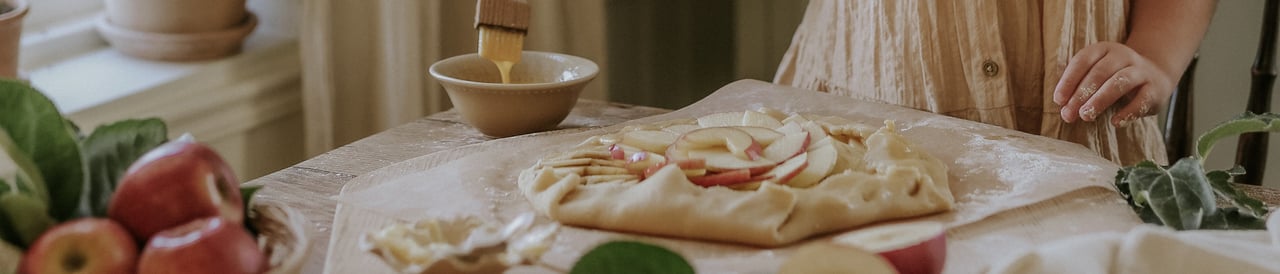 A young girl prepares an apple tart with sliced apples at a kitchen table.