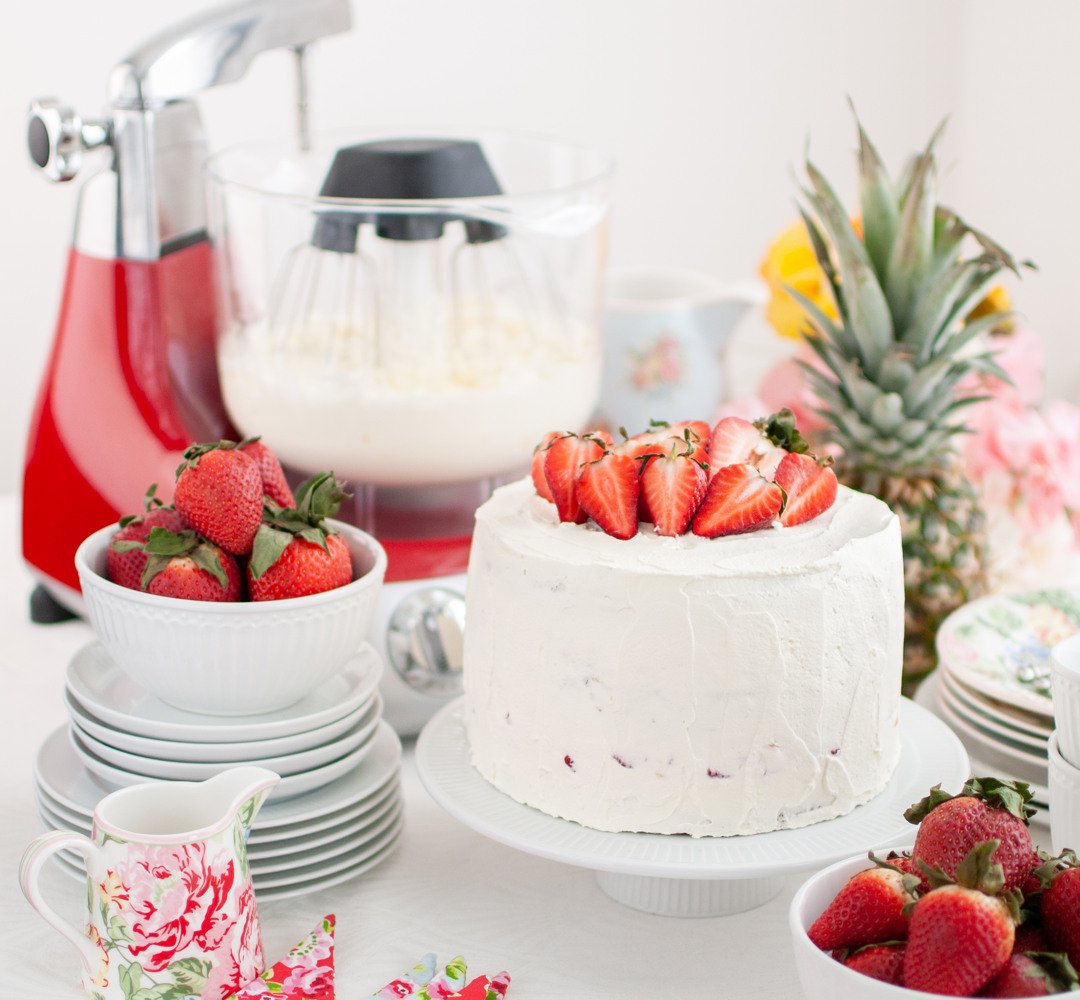 A table topped with a white cake covered in strawberries.