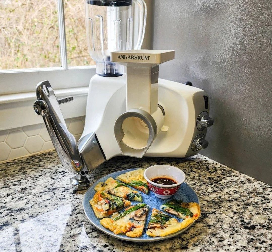 Ankarsrum Assistent with the blender and vegetable cutter attached. A plate of crêpes stands in front.