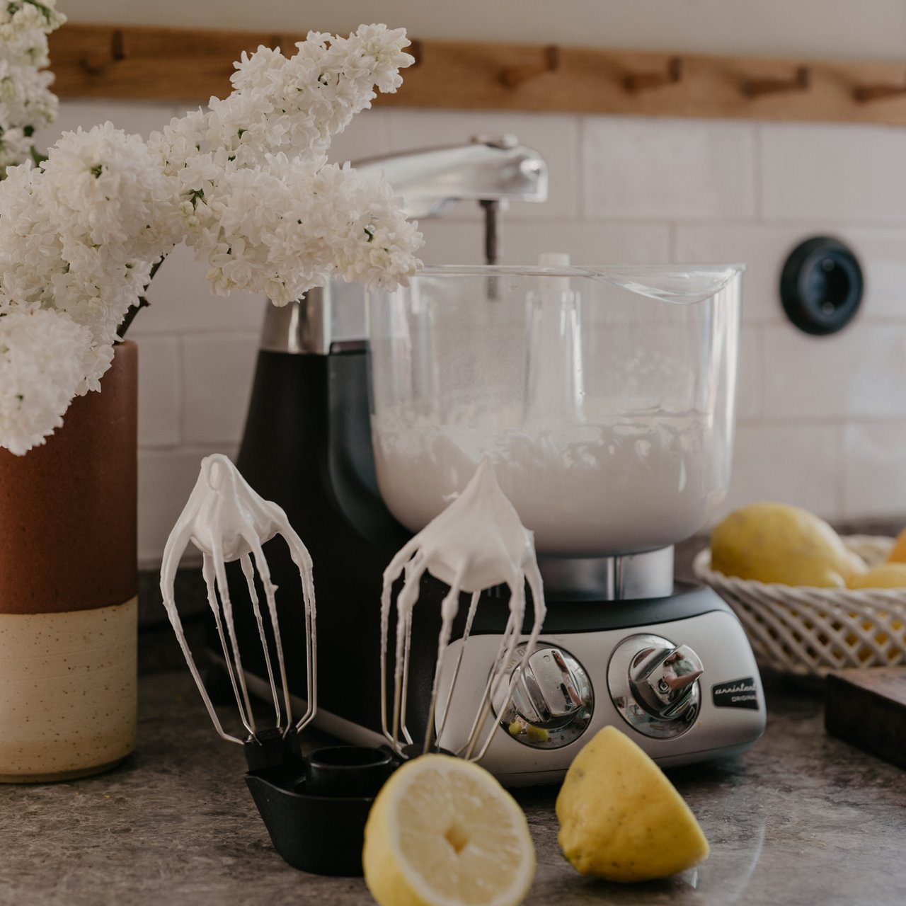 En köksbänk med en mixer, citroner och en vas med blommor.