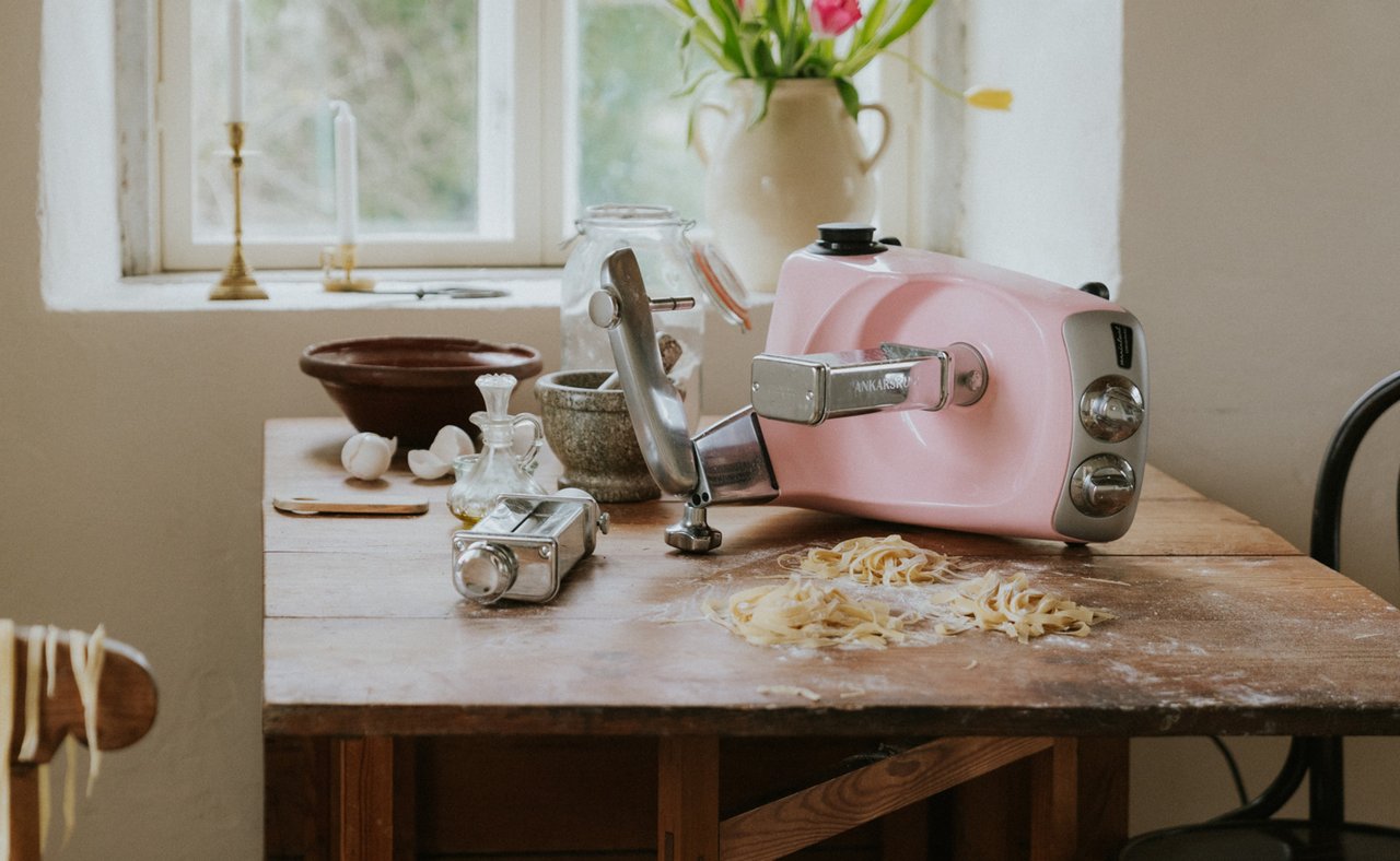 A Cloudy Pink Ankarsrum Assistent Original on a wooden table, making pasta.