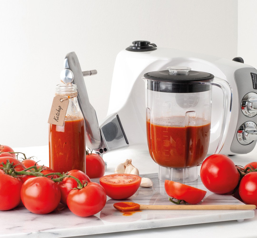 A blender filled with homemade ketchup, next to tomatoes.