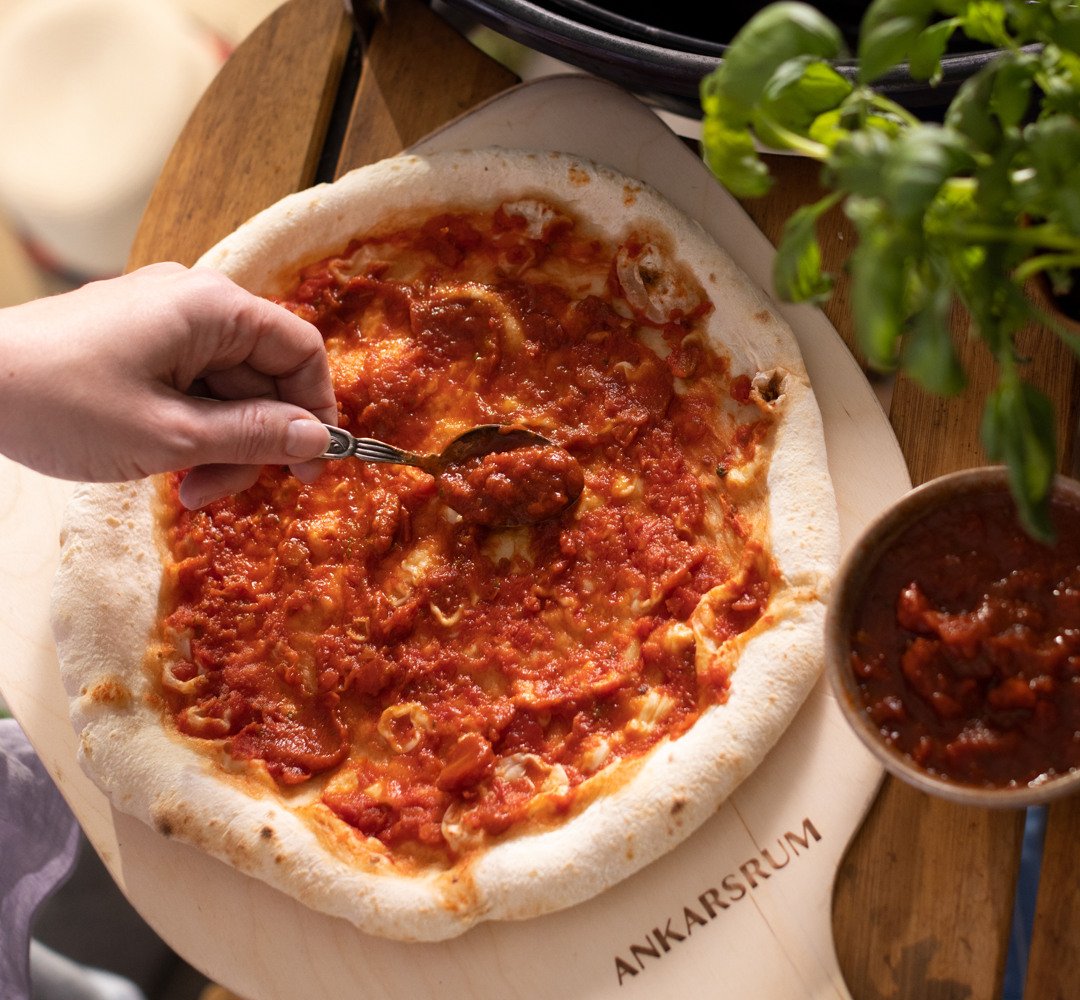 Pizza på en pizzaplåt toppad med tomatsås.