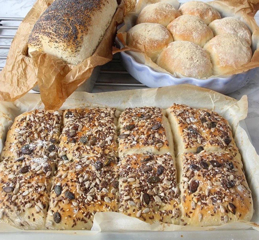 Tre olika typer av bröd på bakplåtar, nybakade och klara.