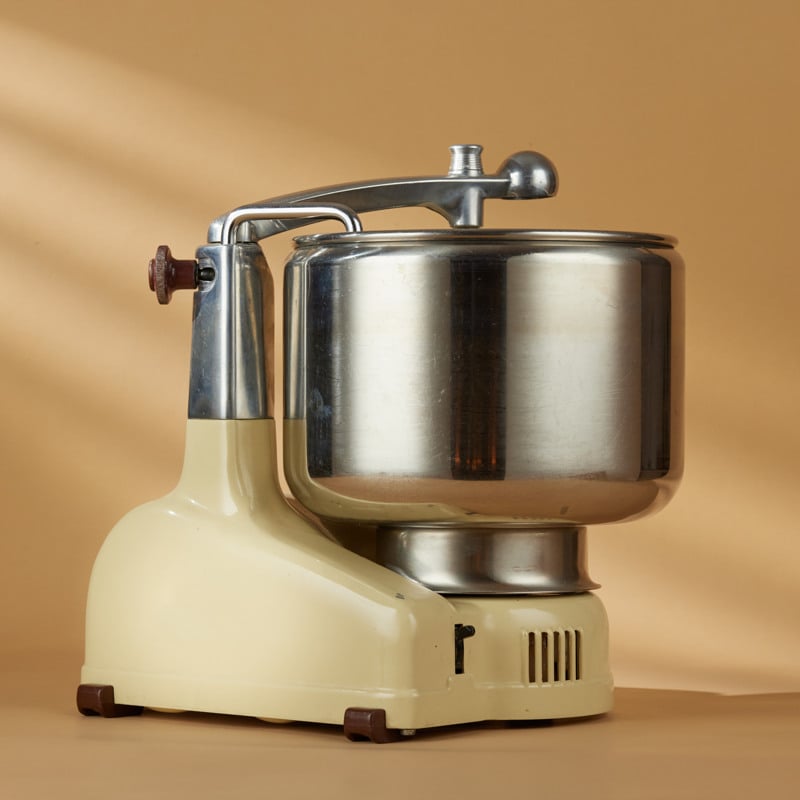 A cream colored older ankarsrum assistent sitting on top of a table.