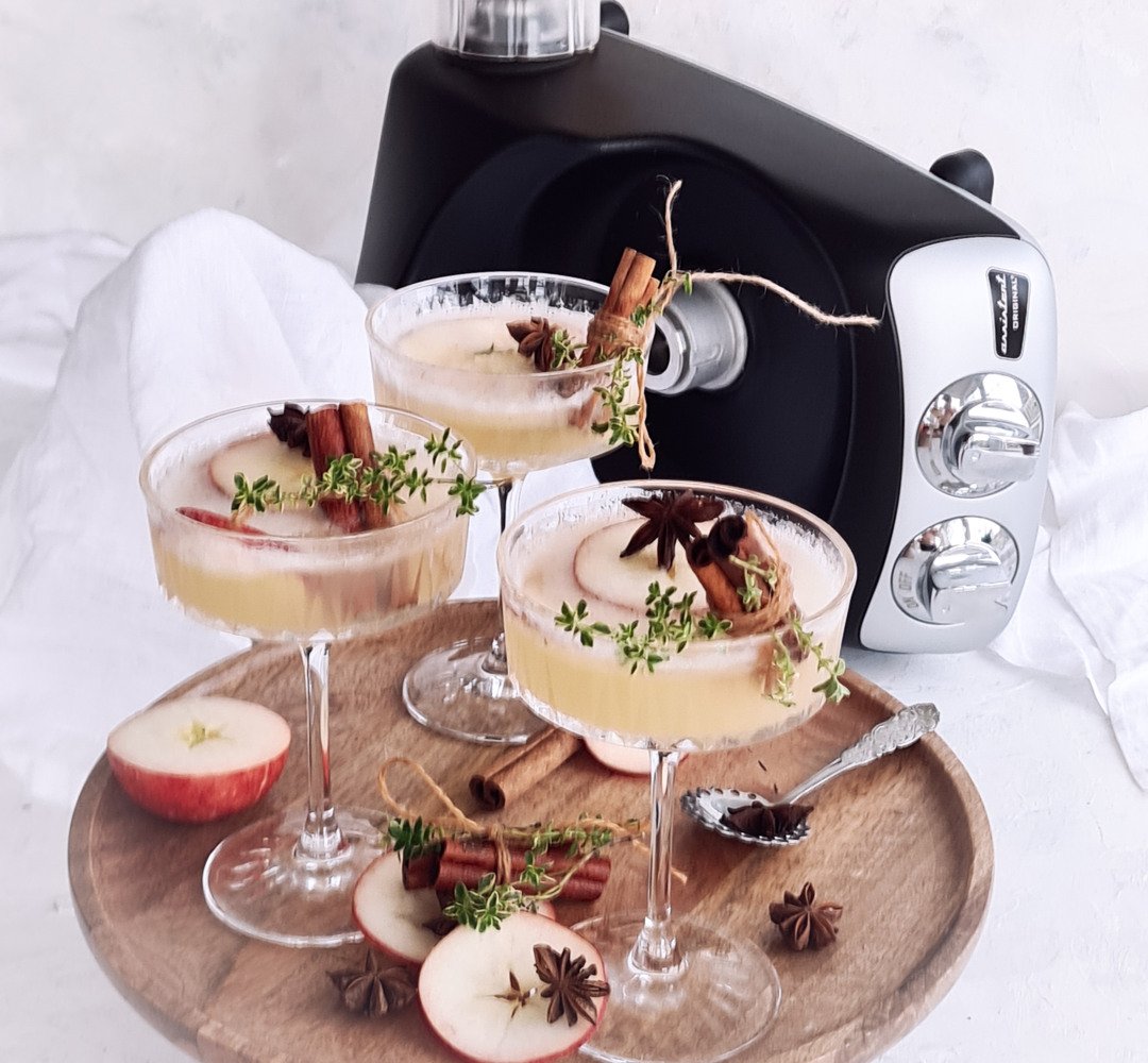 A wooden tray topped with glasses filled with drinks. Sliced apples on the side.