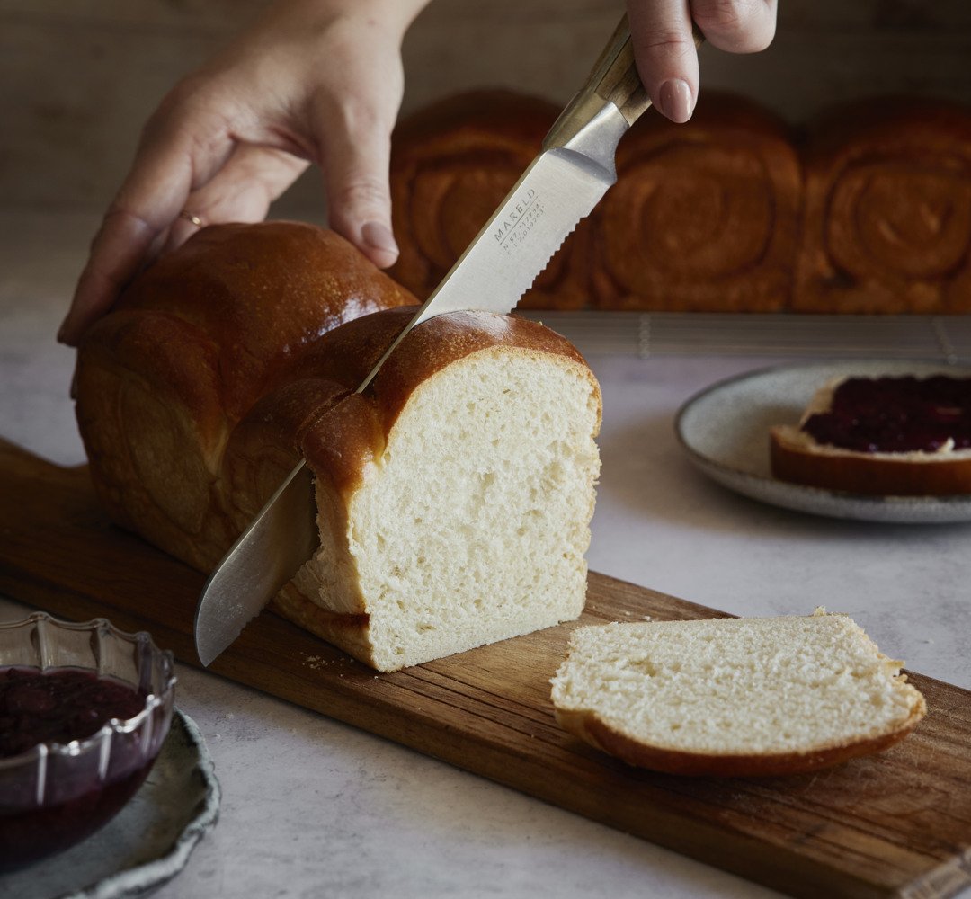 A person cutting a loaf of bread on a cutting board.