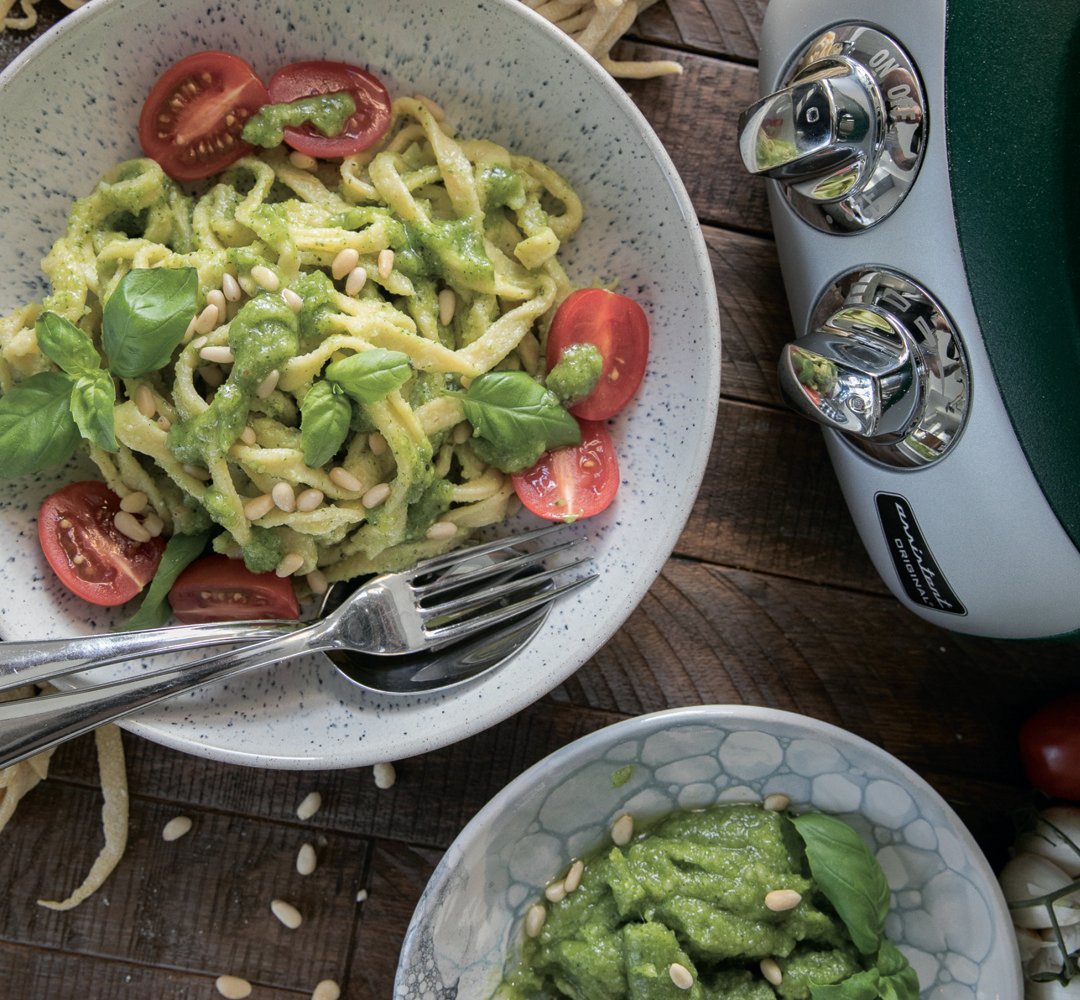 A bowl of pasta with pesto and tomatoes.