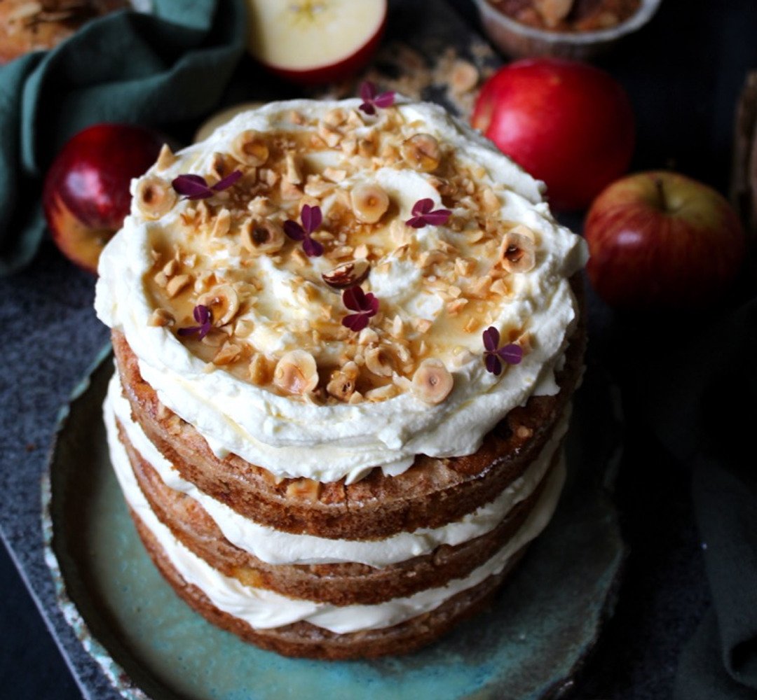 A cake sitting on top of a blue plate. Apples in the background