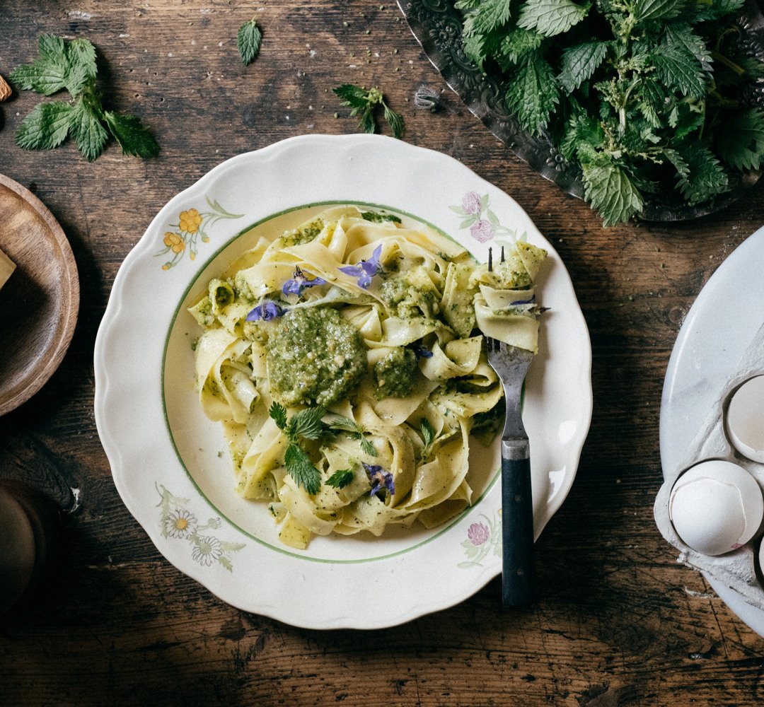 A plate of nettle pesto pasta on a wooden table, with a fork twirling some of the pasta.