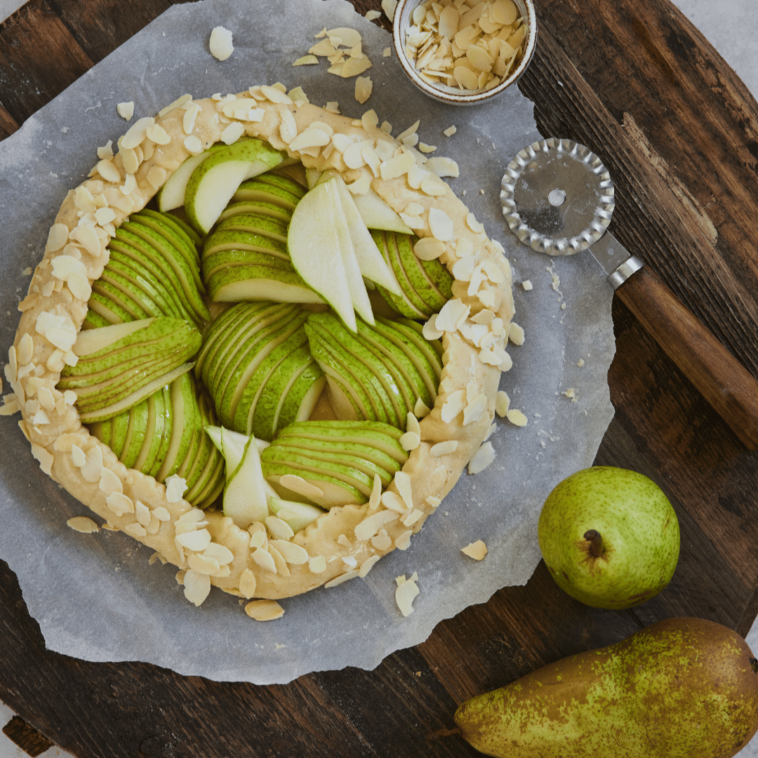 Pärongalette med skivade gröna päron och mandelflarn på ett rustikt träbord.