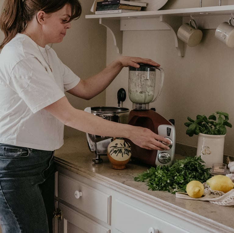 A woman standing in a kitchen preparing food in a blender