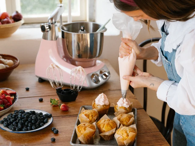 Den bedste røremaskine i farven Cloudy Pink bruges til at sprøjte frosting på muffins på køkkenbord