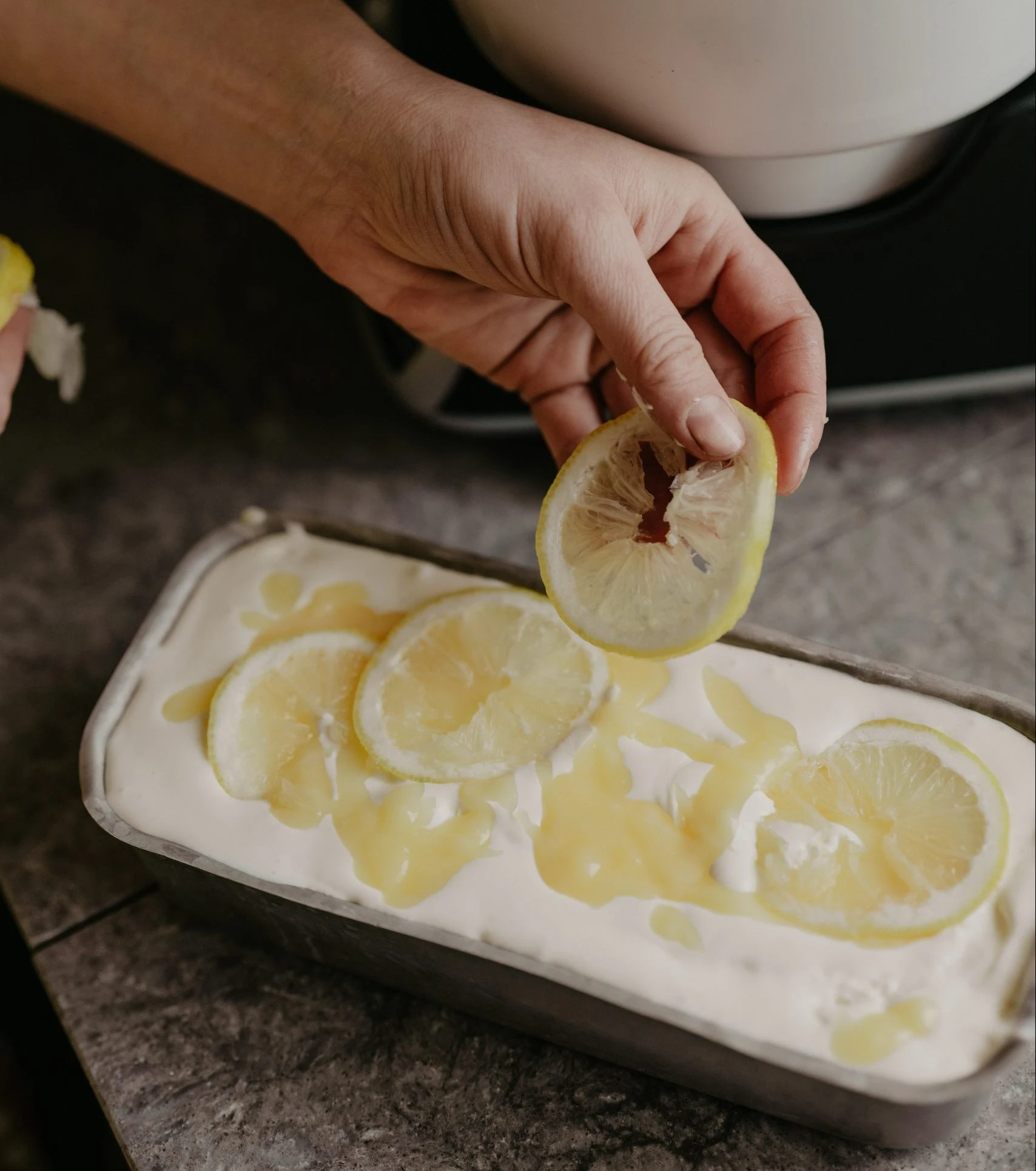 A hand scooping lemon curd ice cream from a container.