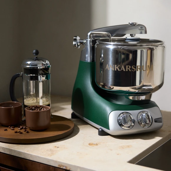 Ankarsrum Assistent Original i farven Forest Green på en lys køkkenbordplade, med en stempelkande og kaffebønner ved siden af.