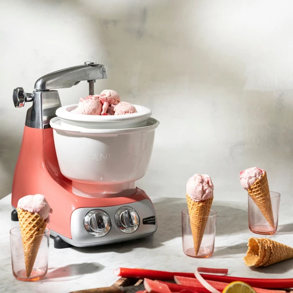 Ankarsrum Assistent Original with the Ice Cream Maker attached in a bright kitchen, with pink ice cream and ice cream cones beside it.