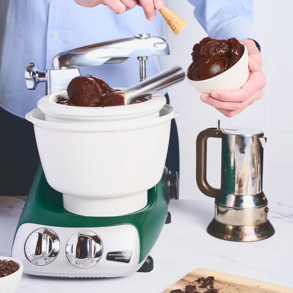 Ankarsrum Assistent Original mit montierter Eismaschine. Eine Person bereitet Schokoladeneis zu und portioniert es in eine Schüssel.