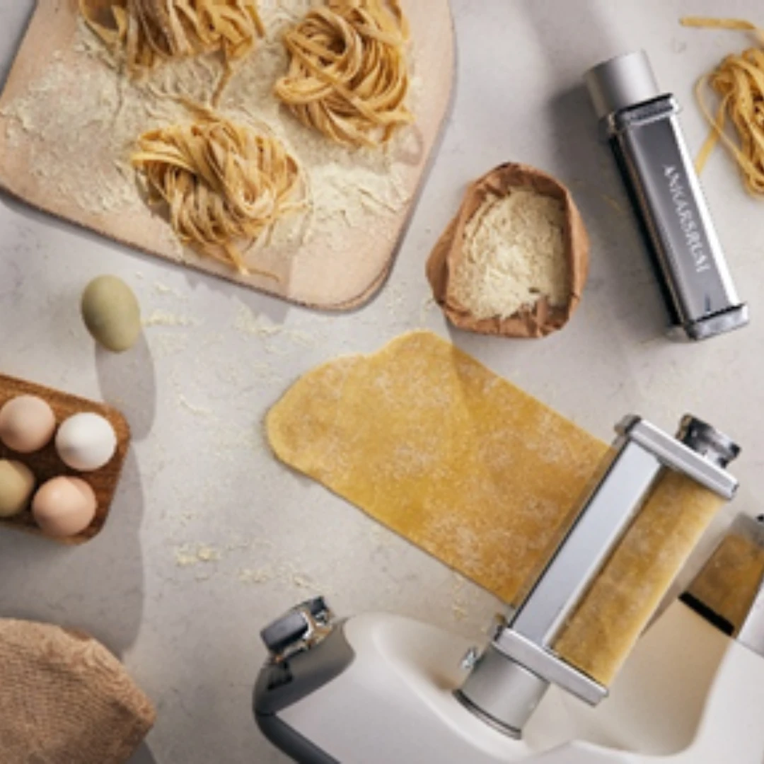 Fersk fettuccine blir til ved hjelp av en pastaskjærer på en robust kjøkkenmaskin, perfekt for ekte italiensk matlaging hjemme.